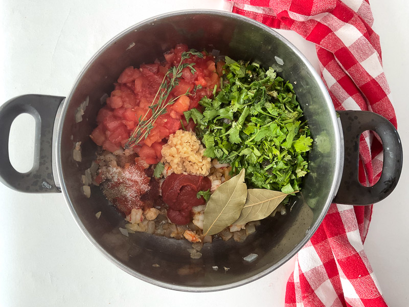 Ajouter l’ail, puis les tomates coupées, la pâte de tomate, les épices, le laurier, le thym frais et la coriandre. Bien mélanger et laisser cuire quelques minutes pour développer les saveurs.