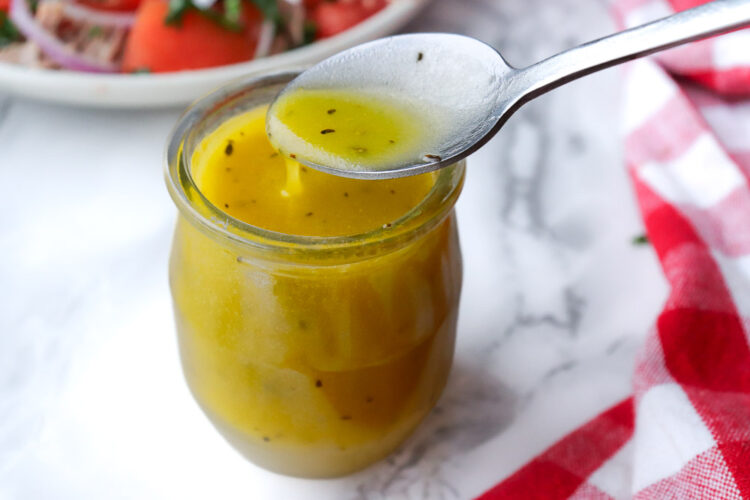 Cuillère servant une vinaigrette méditerranéenne maison au citron et huile d’olive depuis un pot en verre.