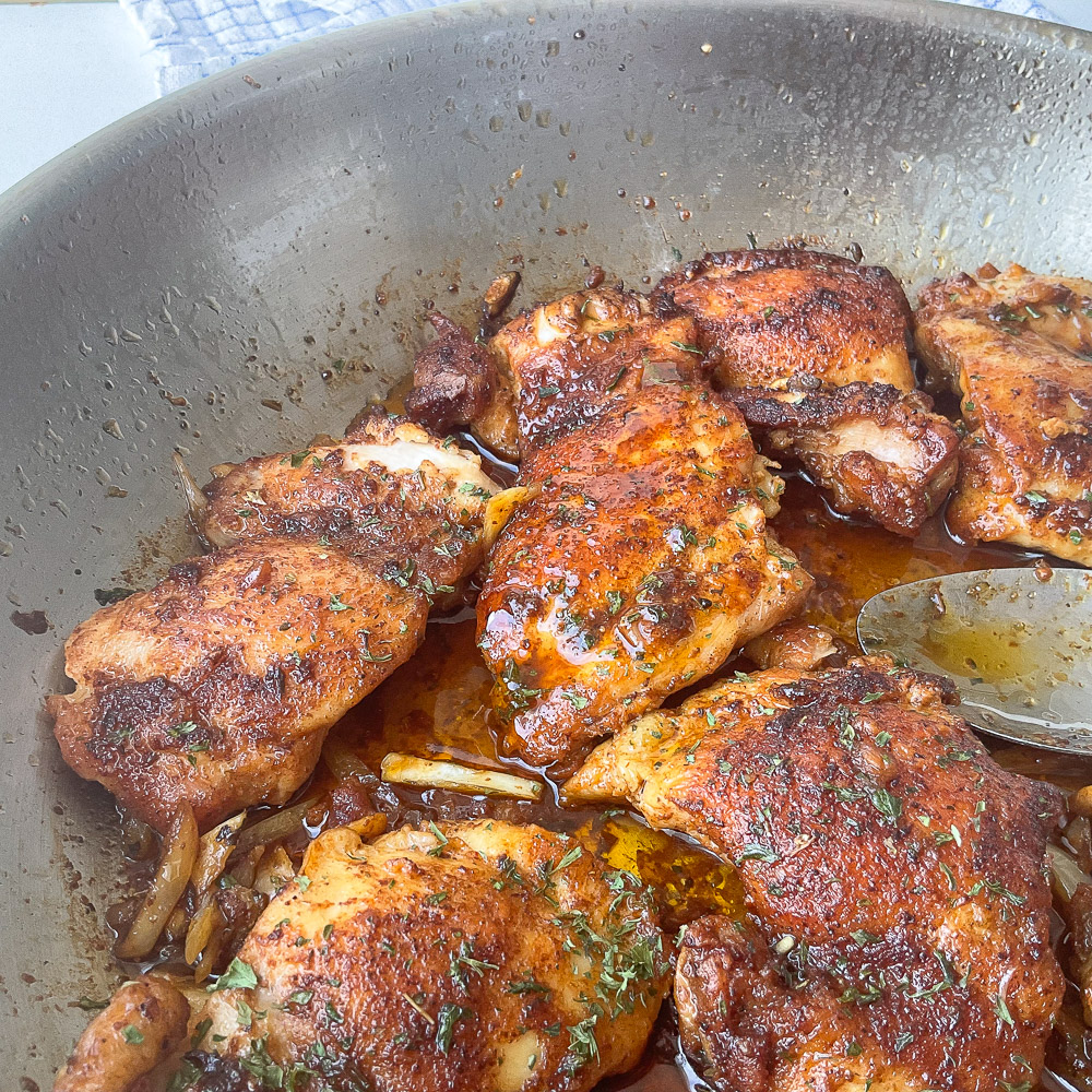 Hauts de cuisses de poulet à l'ail à la poêle dorés et nappés d'une sauce savoureuse, garnis de persil frais et de morceaux d'ail fondants.

