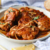 Hauts de cuisses de poulet à l'ail à la poêle servis dans une sauce savoureuse, garnis de bâtonnets d'ail fondants et de persil frais.