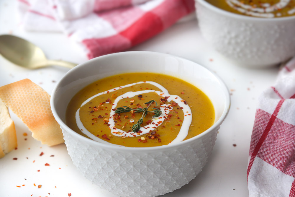 Velouté de courgettes carottes et lentilles rouges servi dans un bol avec filet de crème, pain et torchon