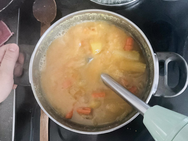 Soupe de légumes et lentilles rouges en cuisson avec mixeur plongeant pour obtenir une texture lisse
