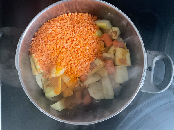 Ajout de lentilles rouges rincées sur des légumes dans une casserole pour un velouté maison