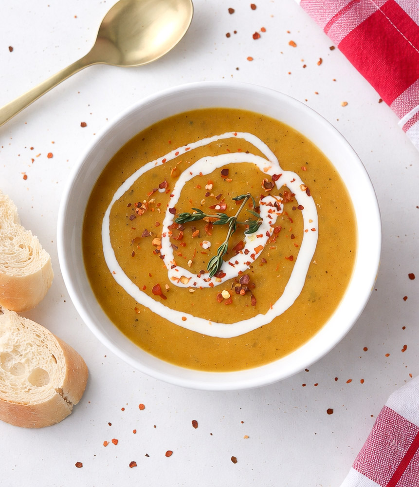 Velouté de courgettes carottes et lentilles rouges servi dans un bol avec filet de crème et flocons de piment