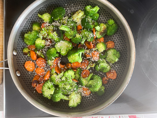 Brocoli et carottes parsemés de graines de sésame dans une poêle avant la fin de la cuisson.