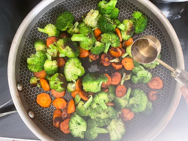 Brocoli et carottes cuisant à la poêle avec une cuillère à soupe d'eau pour attendrir les légumes.