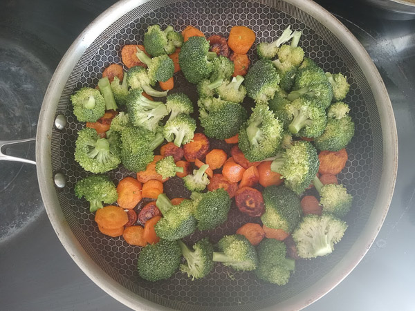 Fleurons de brocoli ajoutés aux carottes dans une poêle pour poursuivre la cuisson des légumes.