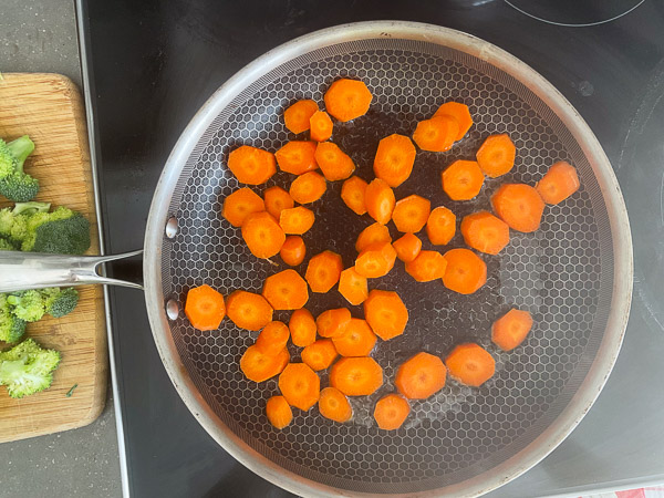 Rondelles de carottes nantaises cuisant dans une poêle avec de l'huile d'olive avant l'ajout du brocoli.