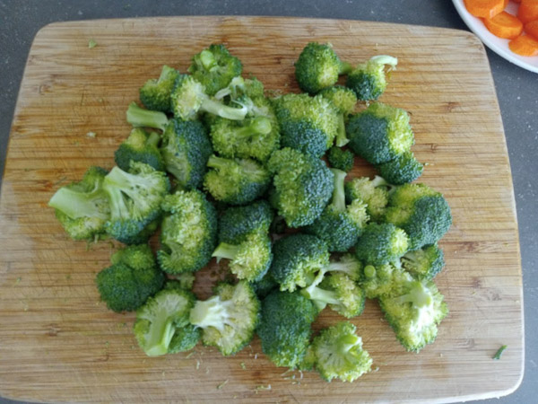 Fleurons de brocoli frais coupés en morceaux de taille similaire sur une planche à découper.