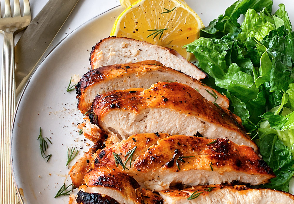 Poitrine de poulet à l’Air Fryer tranchée et servie dans une assiette avec une salade verte et des quartiers de citron. Le poulet est bien doré à l’extérieur et tendre à l’intérieur.