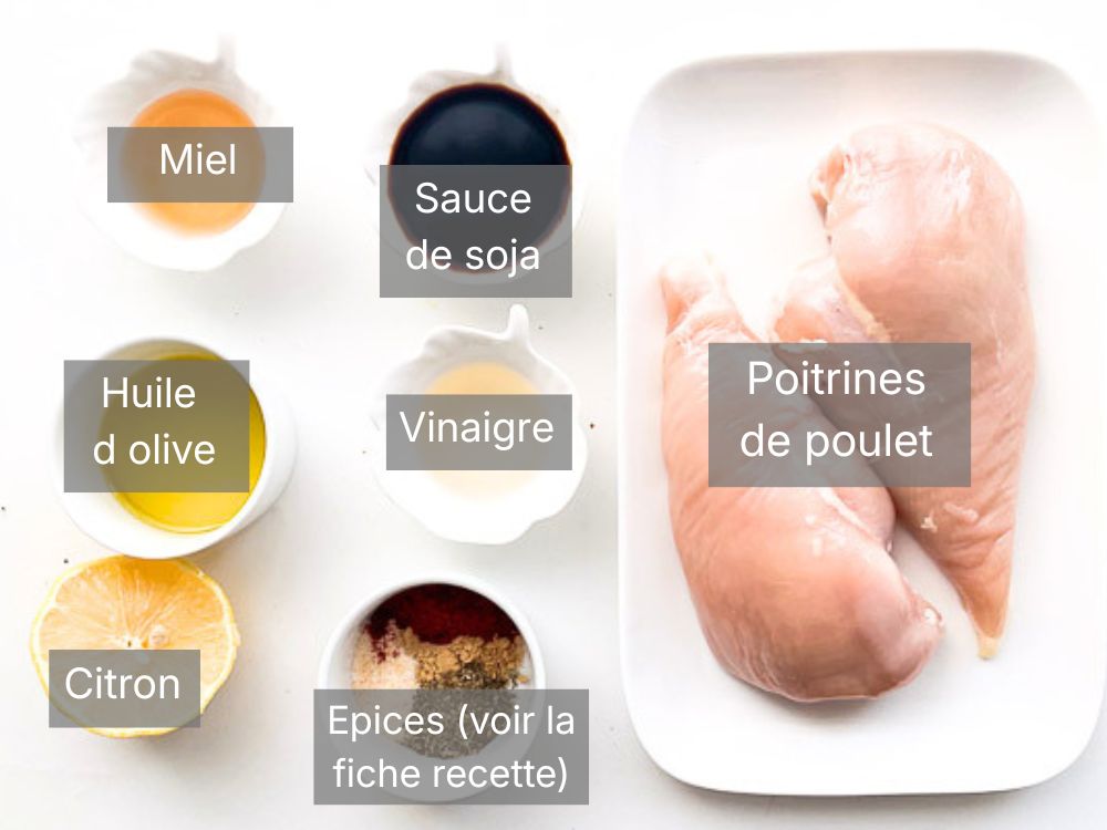Ingrédients pour préparer une poitrine de poulet à l’Air Fryer : poitrines de poulet crues, sauce soja, miel, huile d’olive, vinaigre, citron et mélange d’épices disposés sur un fond clair.