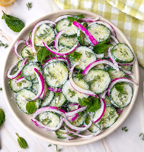 salade aux concombre et oignons rouges avec sa sauce crémeuse a l aneth et feuilles de menthe dans une assiette