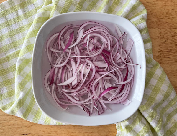 Tranches d’oignon rouge trempant dans un bol d’eau froide afin d’adoucir leur saveur avant la préparation de la salade.