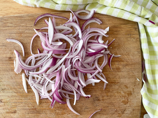 Oignon rouge tranché finement sur une planche à découper en bois, prêt à être utilisé dans une salade de concombre.