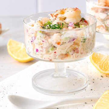 Verrine crémeuse aux crevettes avec céleri, oignon rouge et aneth frais, servie avec des quartiers de citron.