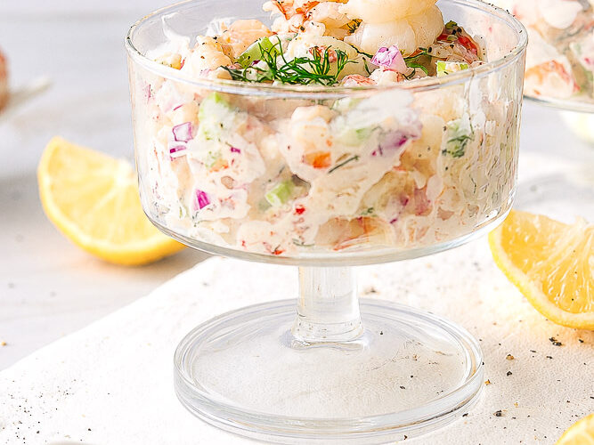 Verrine crémeuse aux crevettes avec céleri, oignon rouge et aneth frais, servie avec des quartiers de citron.
