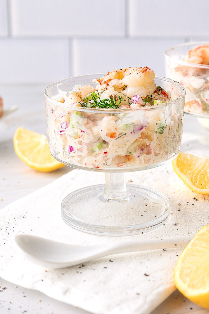 Verrine crémeuse aux crevettes avec céleri, oignon rouge et aneth frais, servie avec des quartiers de citron.