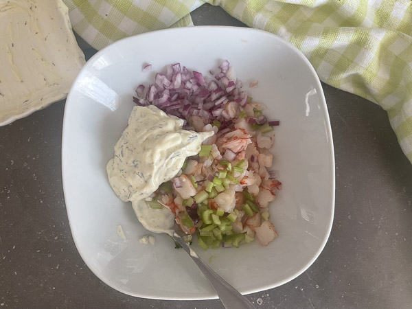 Sauce crémeuse ajoutée aux crevettes, au céleri et à l’oignon rouge dans un grand bol.