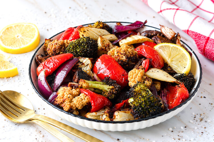 Assiette de légumes marinés rôtis au Air Fryer avec brocoli, chou-fleur, poivron rouge, champignons, oignon rouge et quartiers de citron.