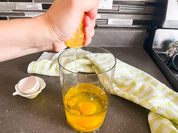 Jus de citron frais ajouté aux ingrédients de la mayonnaise maison dans un récipient pour mélangeur à immersion.