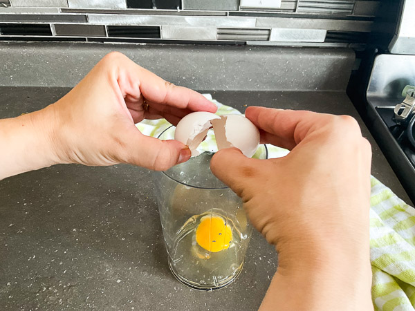 Œuf entier cassé dans un récipient étroit utilisé pour préparer une mayonnaise maison au mélangeur à immersion.