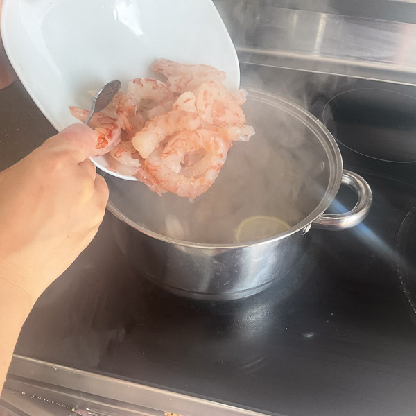 Ajout de crevettes dans une casserole d'eau chaude aromatisée pour les pocher.