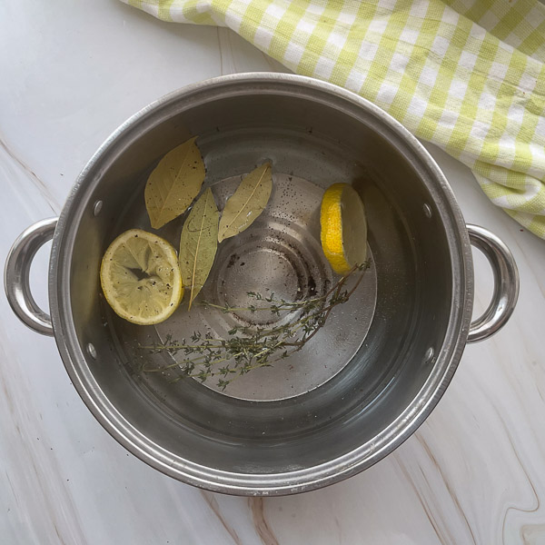 Casserole remplie d'eau avec citron, thym frais, feuilles de laurier, ail, sel et poivre prête pour le pochage des crevettes.
