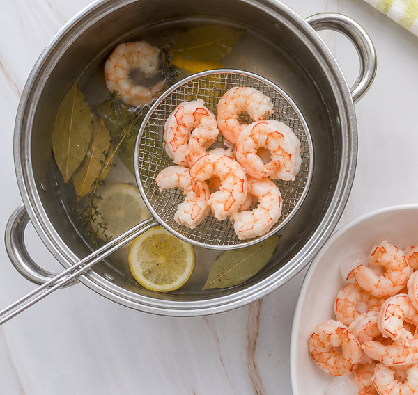 Crevettes pochées retirées de l'eau de cuisson à l'aide d'une écumoire après avoir atteint une texture tendre et juteuse.