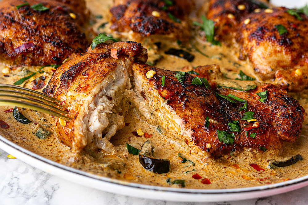 Gros plan sur un haut de cuisse de poulet tendre nappé d’une sauce crémeuse épicée aux jalapeños et garni de persil frais