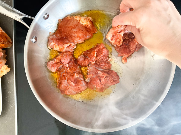 Ajout des hauts de cuisse de poulet assaisonnés dans une grande poêle chaude
