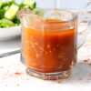 Vinaigrette maison au paprika fumé et à l’ail servie dans un petit pichet en verre, avec salade verte fraîche et gousses d’ail en arrière-plan.